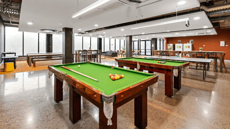 Two pool tables with cues and balls in a large indoor recreation area.