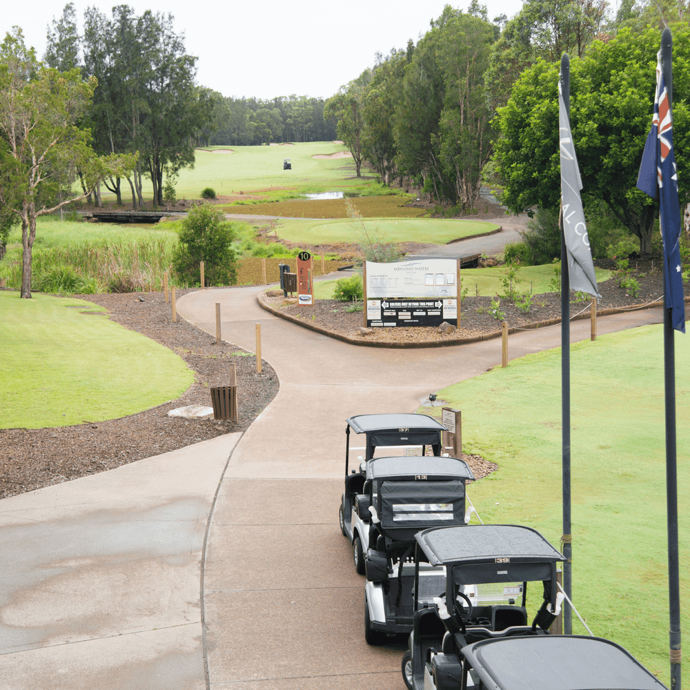 Row of golf carts at golf course entrance with green fairways and trees at Mercure Kooindah Waters