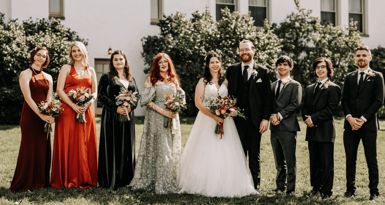 Wedding party in colorful gowns and dark suits standing on the lawn by the white manor at La Tourelle Inn and Spa