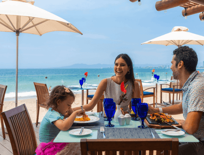 Family dining at Sunset Restaurant with glassware & umbrella shades overlooking the sea at Buenaventura Grand Hotel and Spa
