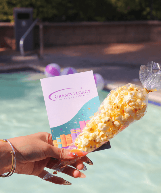 Hand holding a popcorn bag and branded card by a turquoise pool at Grand Legacy at The Park Anaheim
