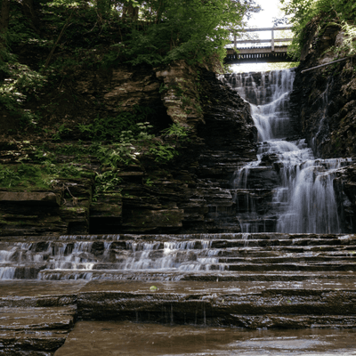 Cascading waterfall over layered rock formations with a wooden bridge overhead near La Tourelle Hotel and Spa