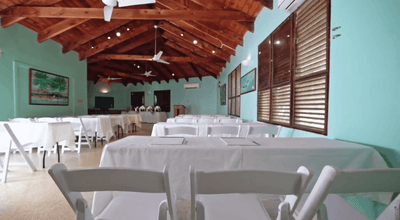 Hibiscus Room with white cloth tables and folding chairs under wood beam ceiling at Emerald Beach Resort