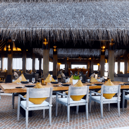 Overwater restaurant with thatched roof and white chairs set for Thanksgiving in the Maldives