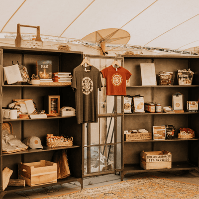 Retail display with branded shirts hanging on a rack and gift items on shelves at the La Tourelle Hotel and Spa tent shop