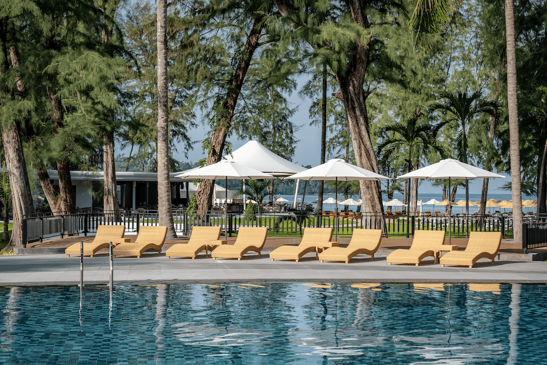 Sunbeds by the outdoor pool area on a sunny day with an ocean backdrop at Amora Hotel
