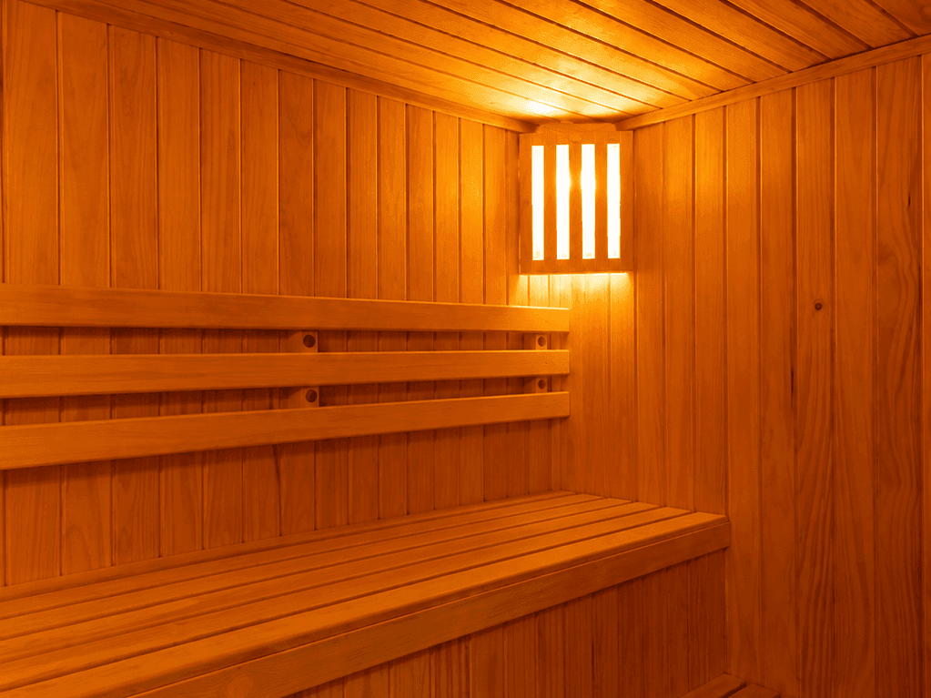 Interior de sauna de madera con bancos escalonados y cálida lámpara de pared en Veranda Hotel