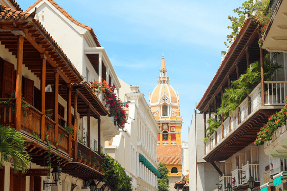 Calle colonial con balcones de madera y flores que enmarca una iglesia con cúpula amarilla en Hotel Charleston Santa Teresa