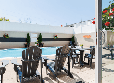 Black patio lounge chairs surrounding an outdoor dining table beside a swimming pool in sunshine at Rodd Moncton