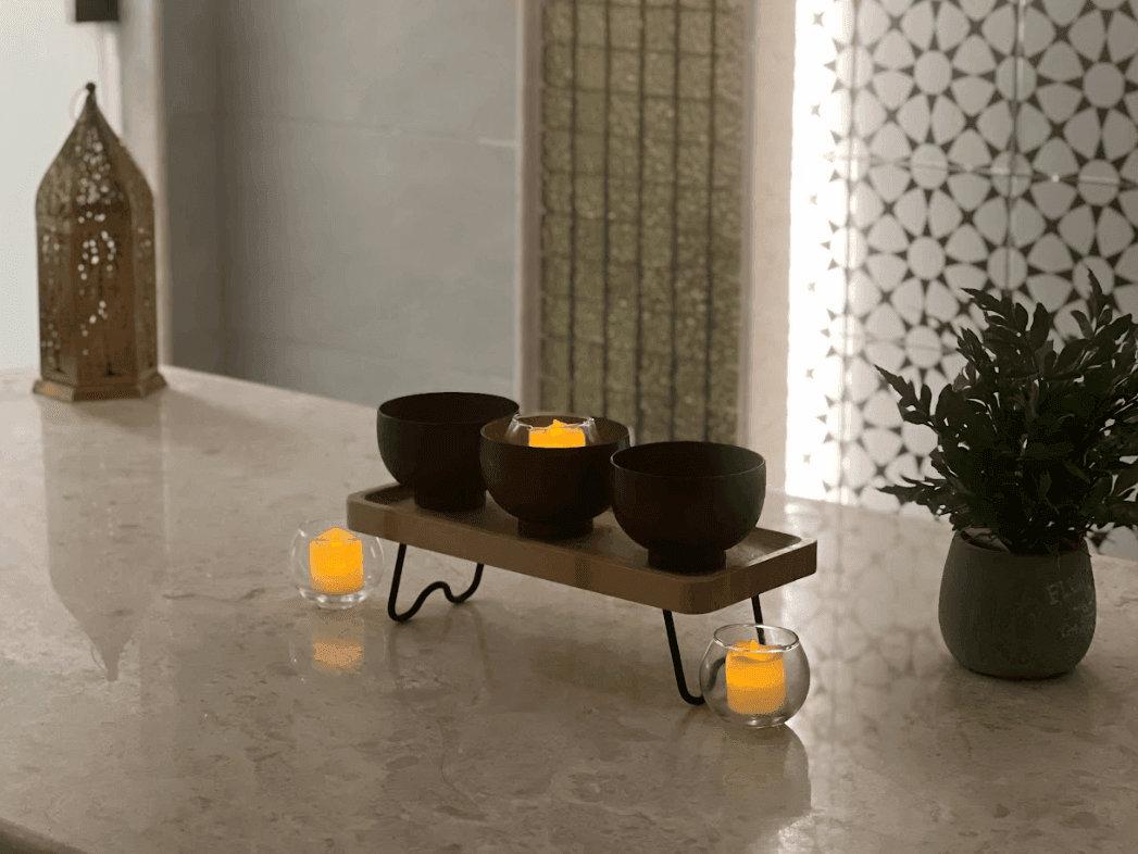 Candle bowls on a tray by a plant on a marble counter, spa near a gold lantern at Warwick Al Jubail