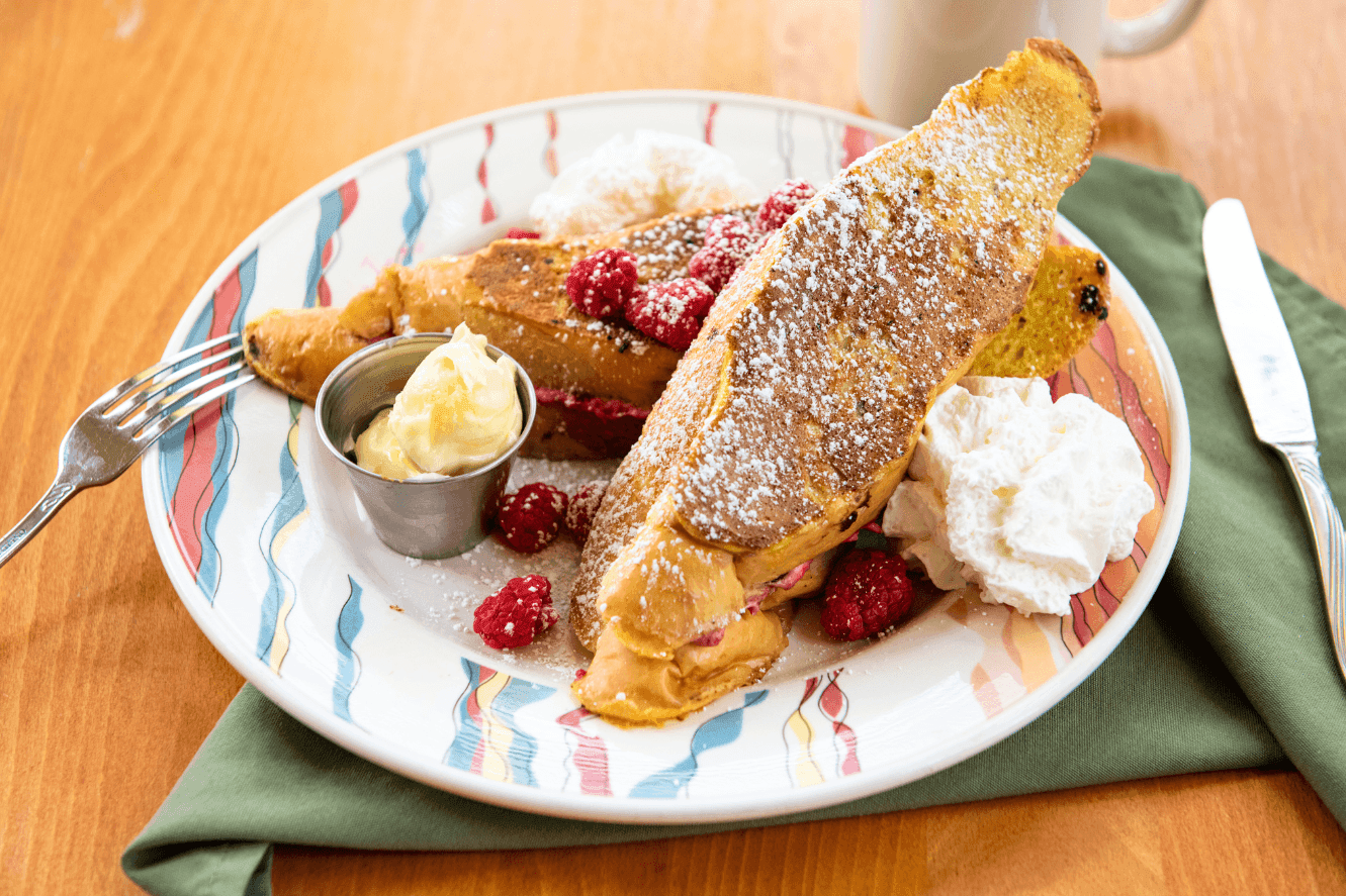 a plate of french toast with butter, whipped cream, and raspberries