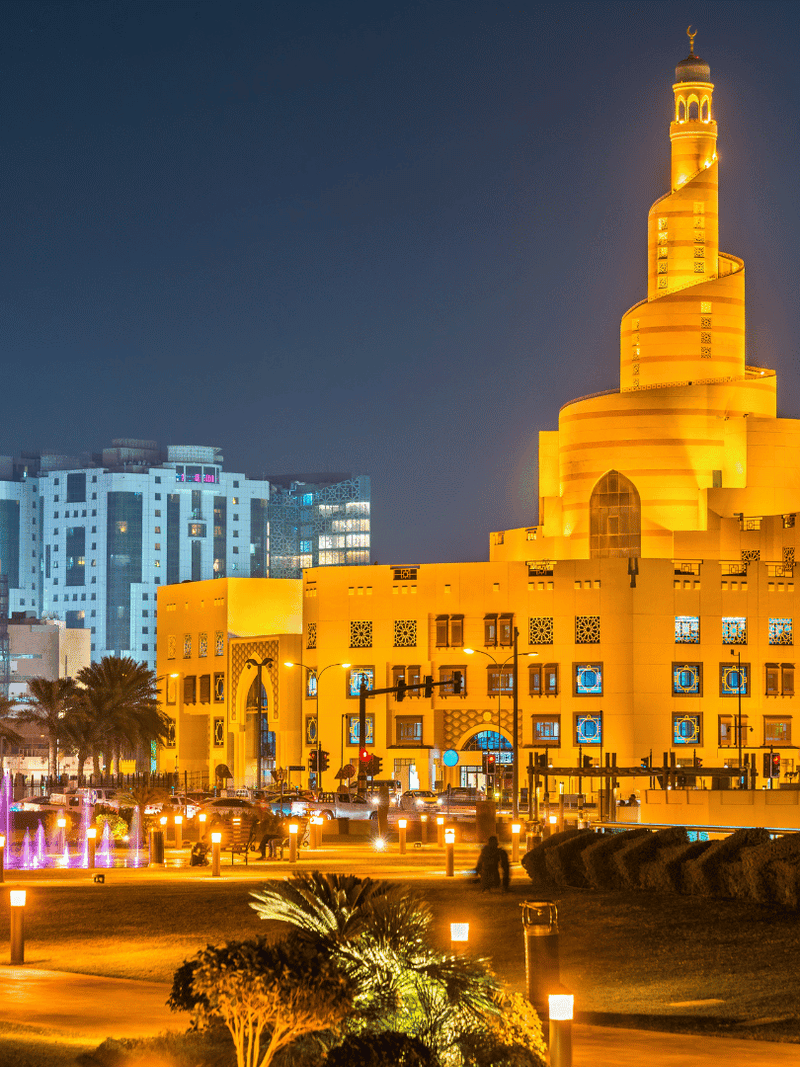 Illuminated Souq Waqif with a prominent central tower at night in an urban setting.