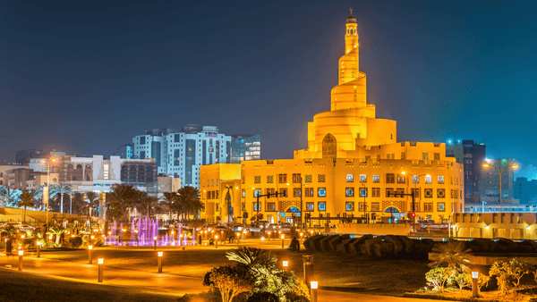 Illuminated Souq Waqif with a prominent central tower at night in an urban setting.
