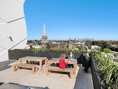Students sitting on rooftop terrace with wooden benches, greenery, and city skyline views at Student Living - Vivida