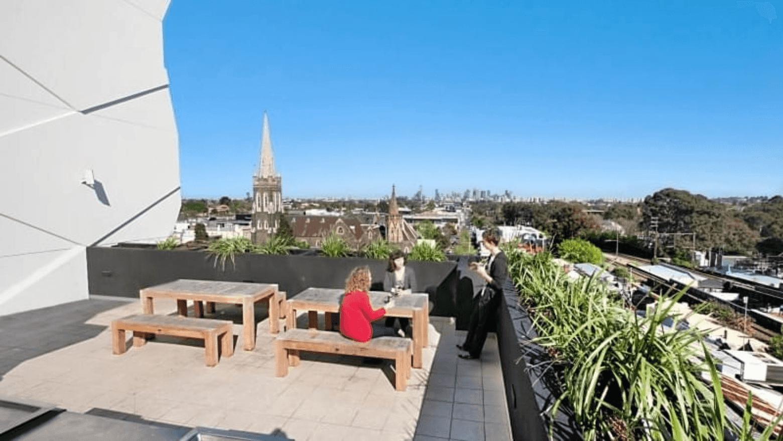 Students sitting on rooftop terrace with wooden benches, greenery, and city skyline views at Student Living - Vivida