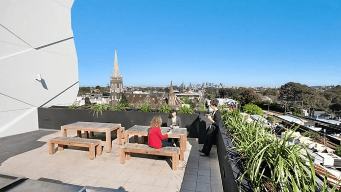 Students sitting on rooftop observation deck with wooden seating and city skyline views at Student Living Vivida