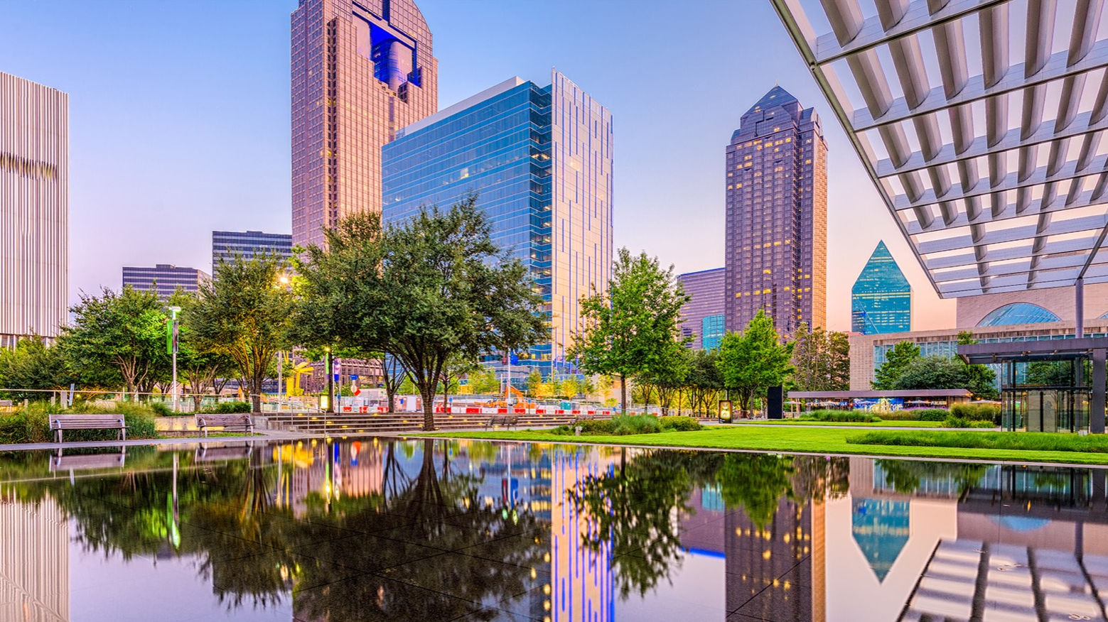 Skyline of Dallas, showcasing modern buildings and lush greenery reflected in a serene pond near Warwick Hotels and Resorts