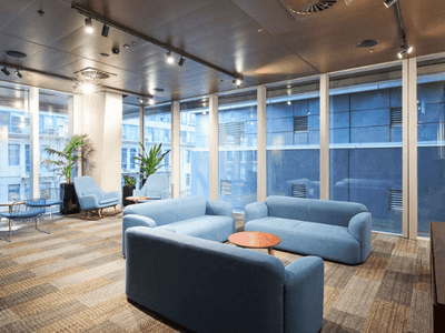 Modern lounge with blue couches, large windows, and a mounted TV.