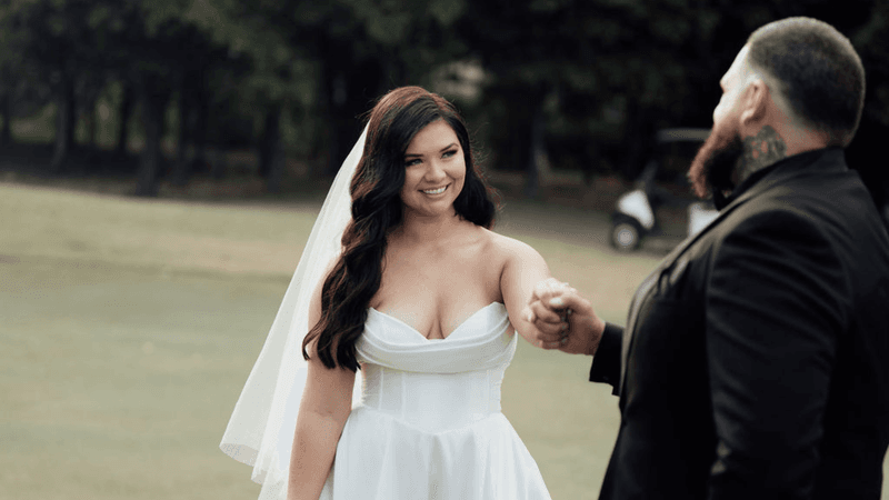 Bride and groom holding hands, smiling on a grassy field with trees in the background for 2026 elopement packages.