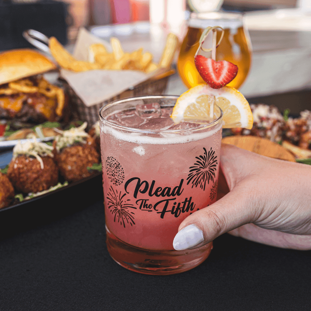 a hand holding a glass with a pink drink and a strawberry garnish