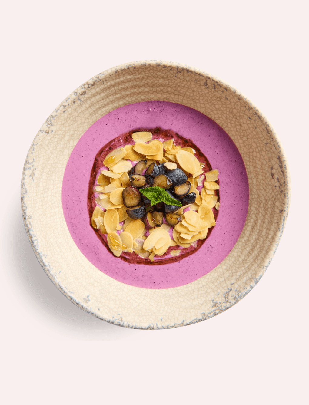 A vibrant purple smoothie bowl topped with fresh blueberries, sliced almonds, and a mint leaf served at The Londoner Hotel