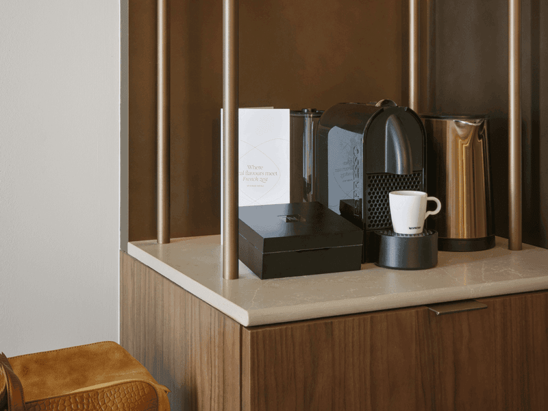 Hotel room coffee station with wooden cabinet, coffee maker, cups and brewing accessories