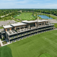 Aerial view of a golf practice facility with tiered bays, putting greens, and a large pond near Star Suites Vero Beach