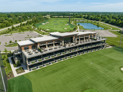 Aerial view of a golf practice facility with tiered bays, putting greens, and a large pond near Star Suites Vero Beach