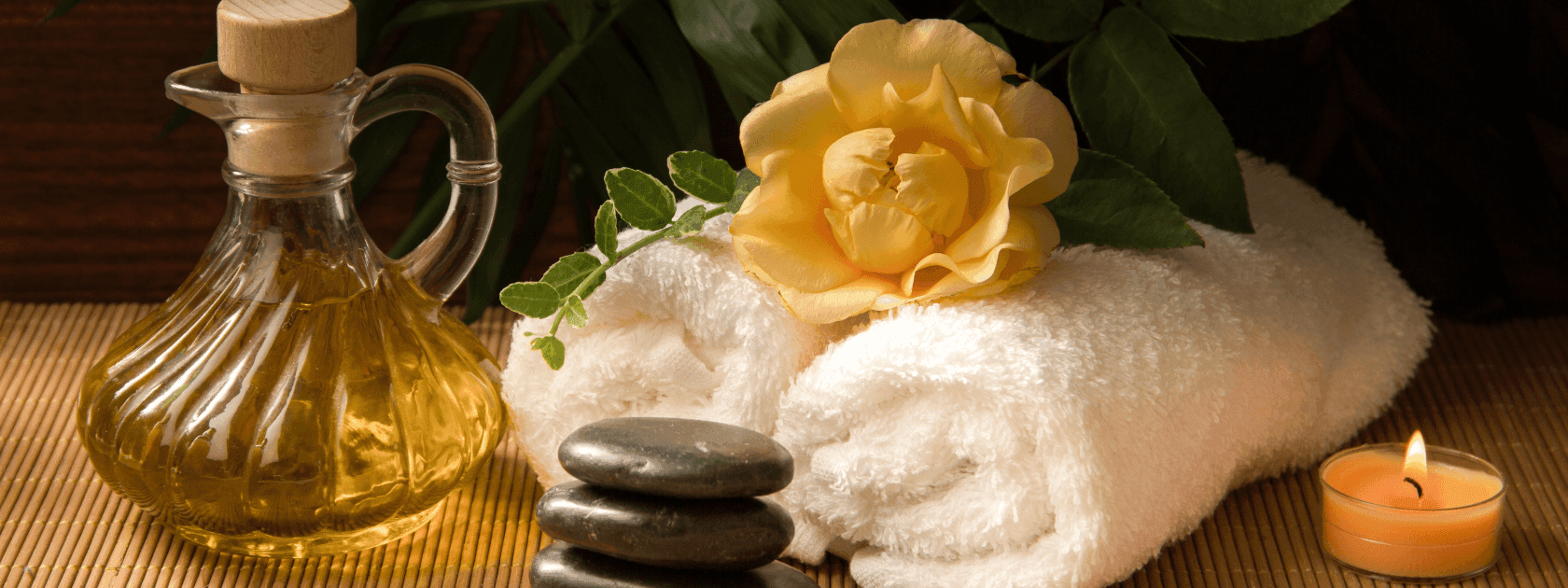 Spa setting with a massage oil bottle, white towels, stones, a yellow rose, and a lit candle at Polonia Palace Hotel