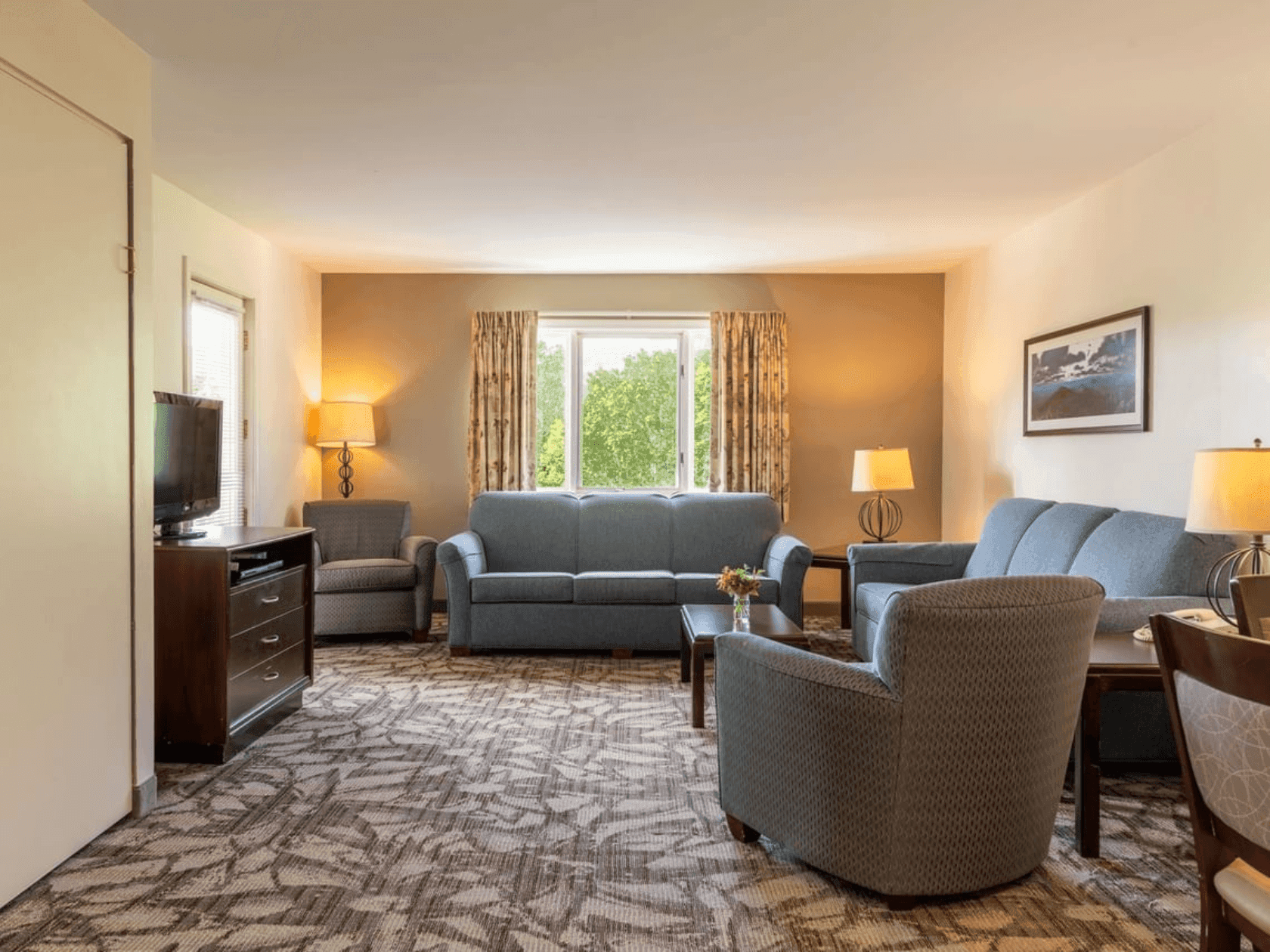 The living room of the premium suite with two couches, two chairs, a coffee table, a TV, and two lamps.