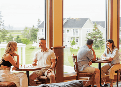 Couples playing indoor board games by large windows at Rodd Crowbush Golf Beach Resort, Prince Edward Island