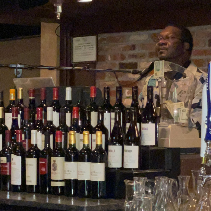 Photo of musician Doug Jennings playing piano at ICONA Windrift Signature Lounge Bar behind rows of wine bottles