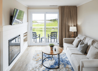 Living room with sofa by coffee table and fireplace overlooking green golf course at Rodd Crowbush Golf & Beach Resort