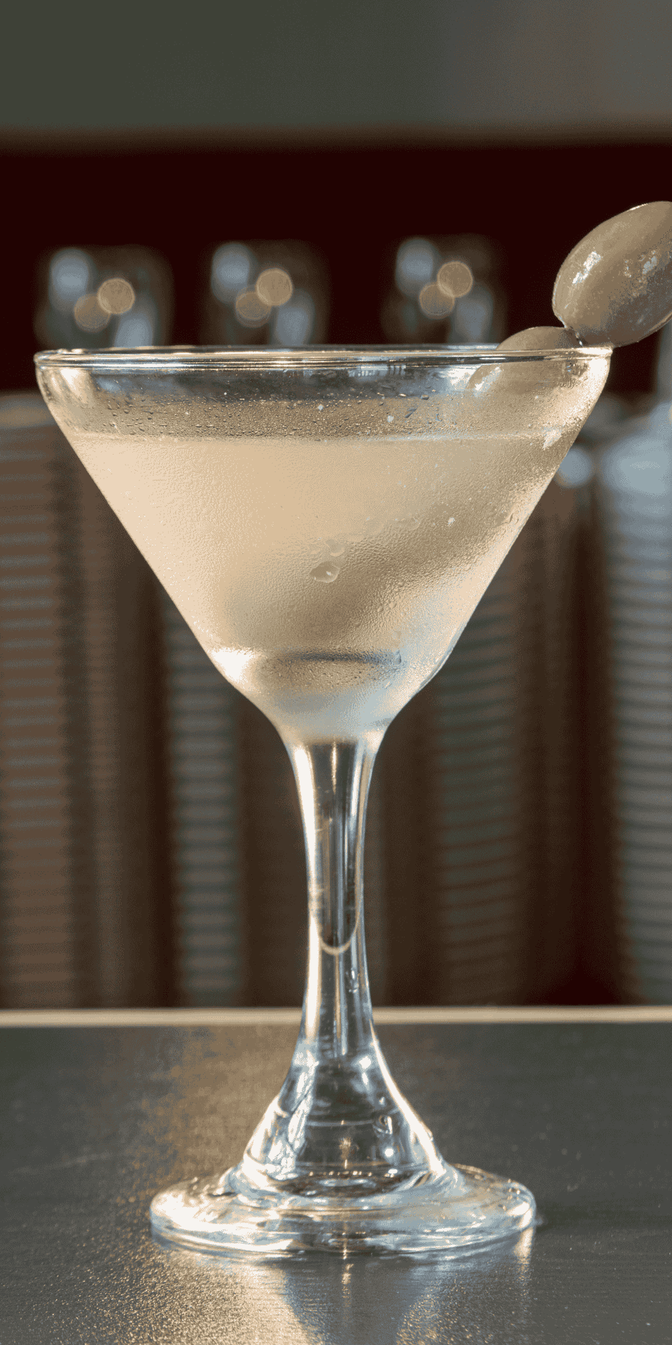 Martini glass with olive garnish resting on the rim, set atop a dim-lit bar counter surface at La Tourelle Inn & Spa