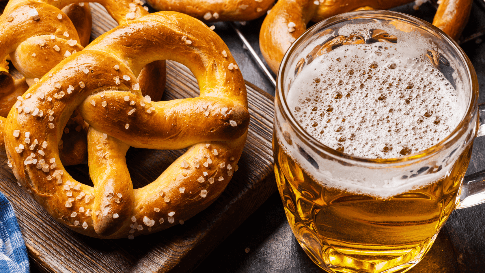 Pretzels on a cutting board and a glass of beer on a dark surface.