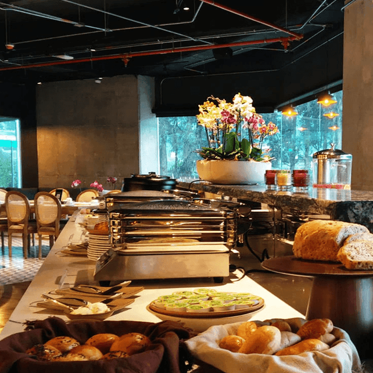 Bufé de desayuno con cestas de pan y bandejas calientes junto a orquídeas en Unika Hotels, restaurante en Bogotá
