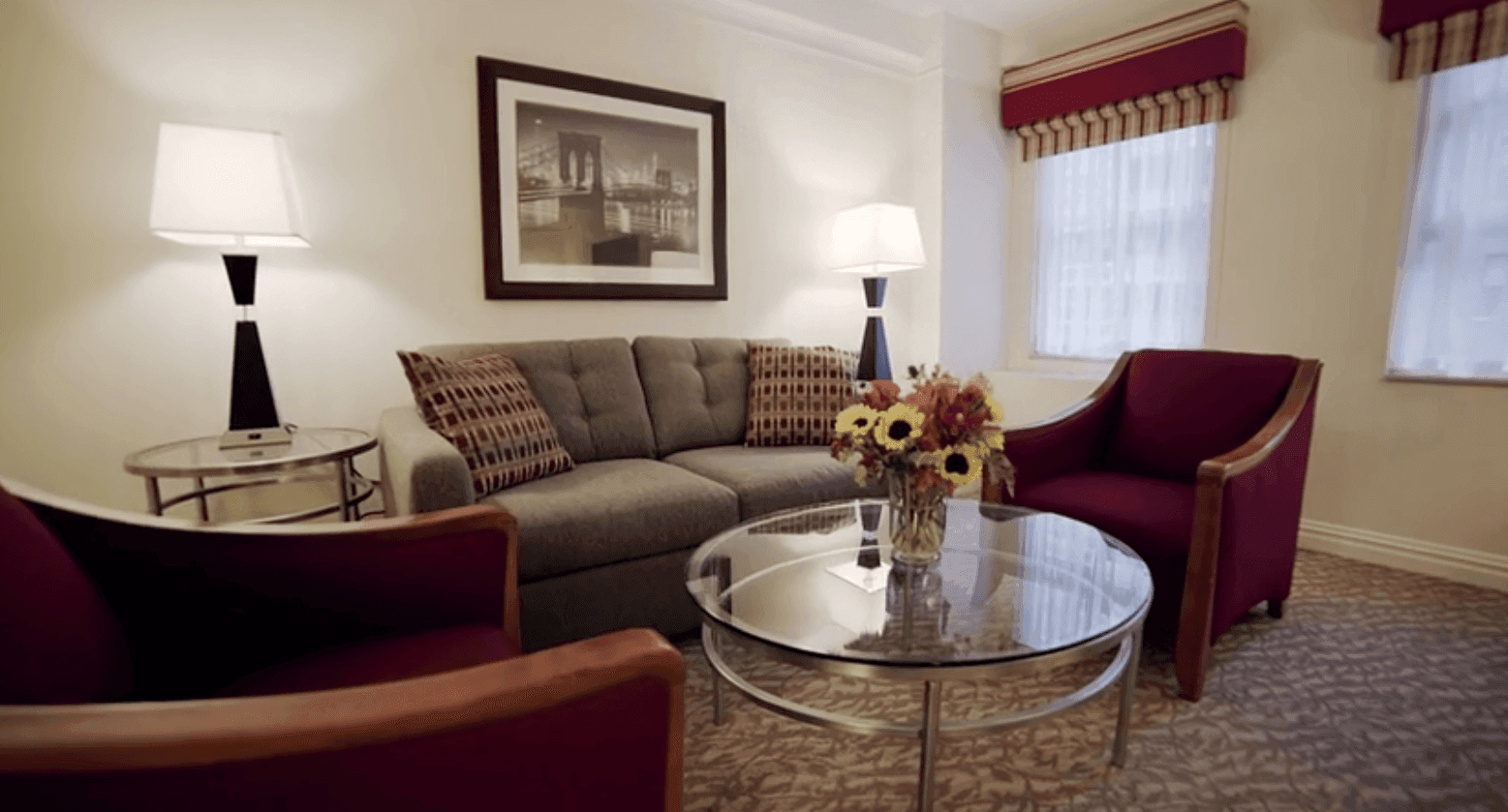 A wide view of a hotel suite's living area with a sofa, armchairs, coffee table, and lamps.