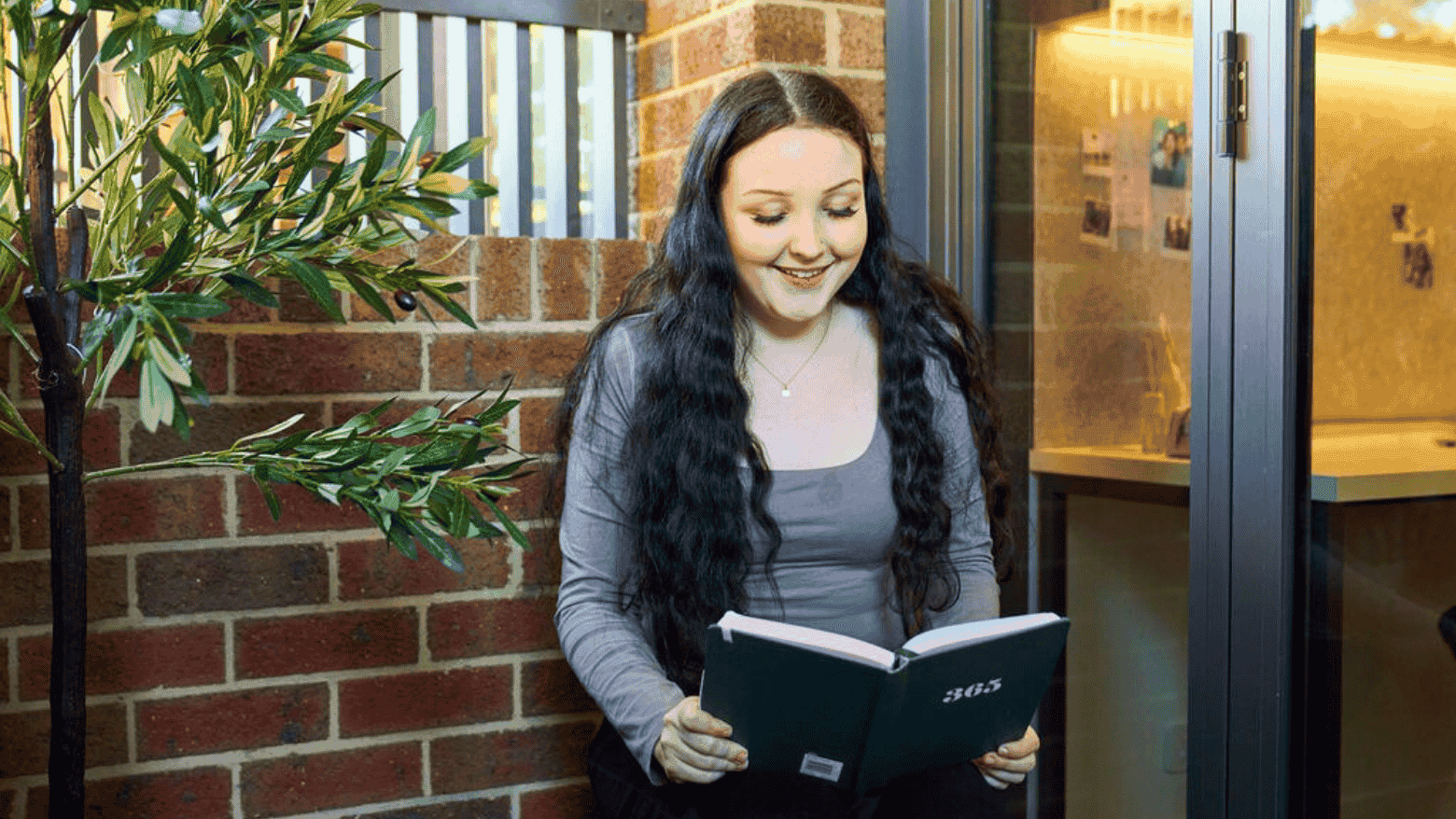 A smiling woman reading a book at UniLodge Royal Melbourne.