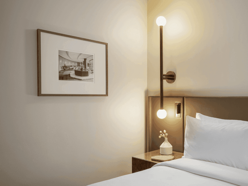 Hotel bedroom with white bedding, framed artwork, bedside lamp and wooden headboard detail