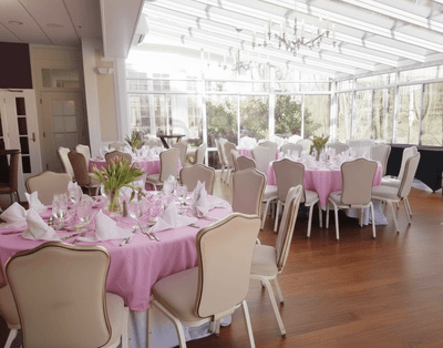 Round dining tables with tablecloths and cream chairs inside a glass room at Avon Old Farms Hotel