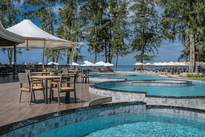 Dining tables by the outdoor pool area on a sunny day overlooking the sea at Amora Hotel
