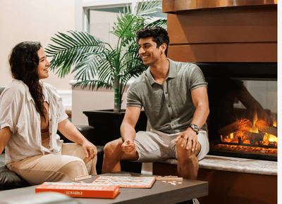 Smiling couple playing a board game on a coffee table by a warm, glowing fireplace in a lounge area at Rodd Hotels & Resorts