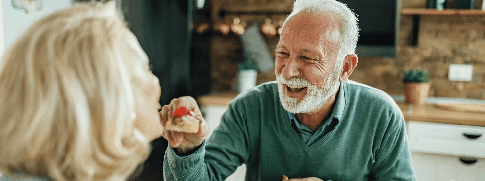 Senior man laughing while being fed a snack by a woman at Novotel Sydney International Airport