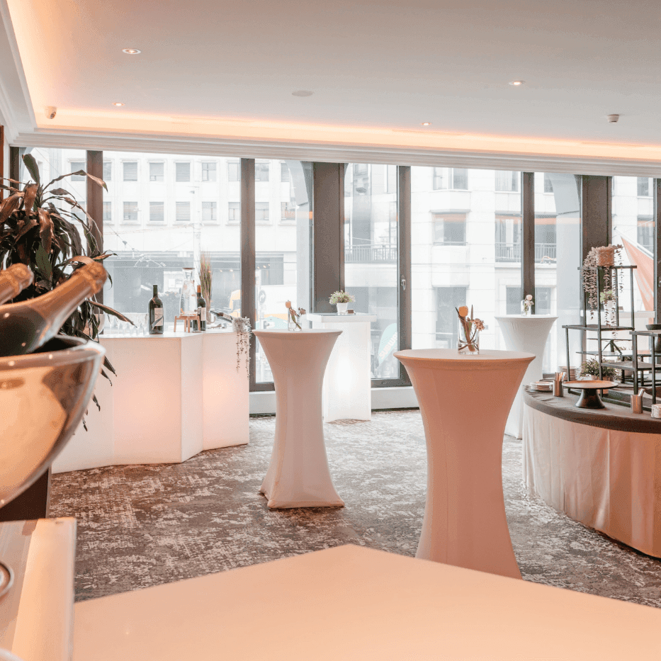 Tall white bistro tables by a curved buffet under soft glow lights in Foyer Mezzanine at Warwick Geneva