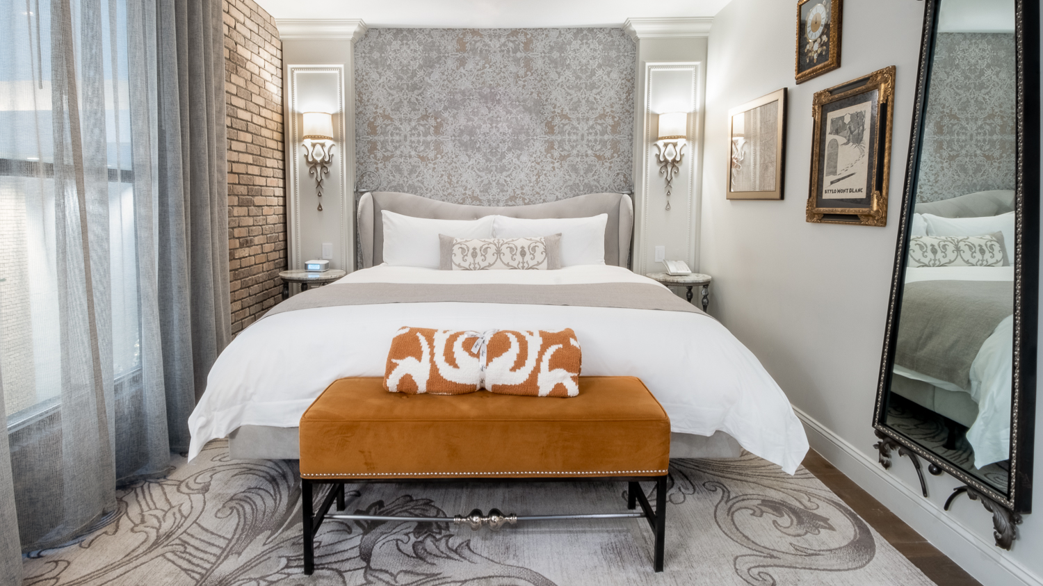 A hotel room with a large bed, a brown bench, and a mirror on the wall