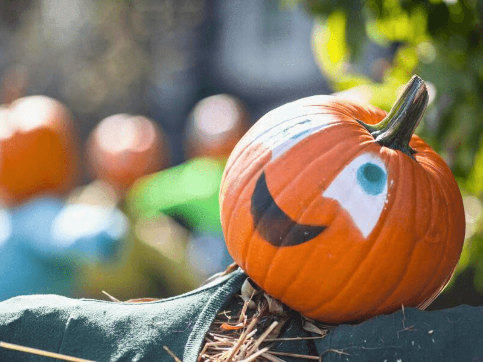 A pumpkin with a smiley face placed on a straw-covered surface with more pumpkins in the background.