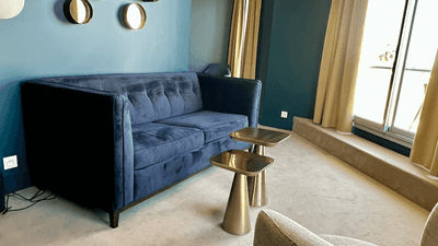 Modern living room with blue couch, two side tables, and a chair facing a large window.