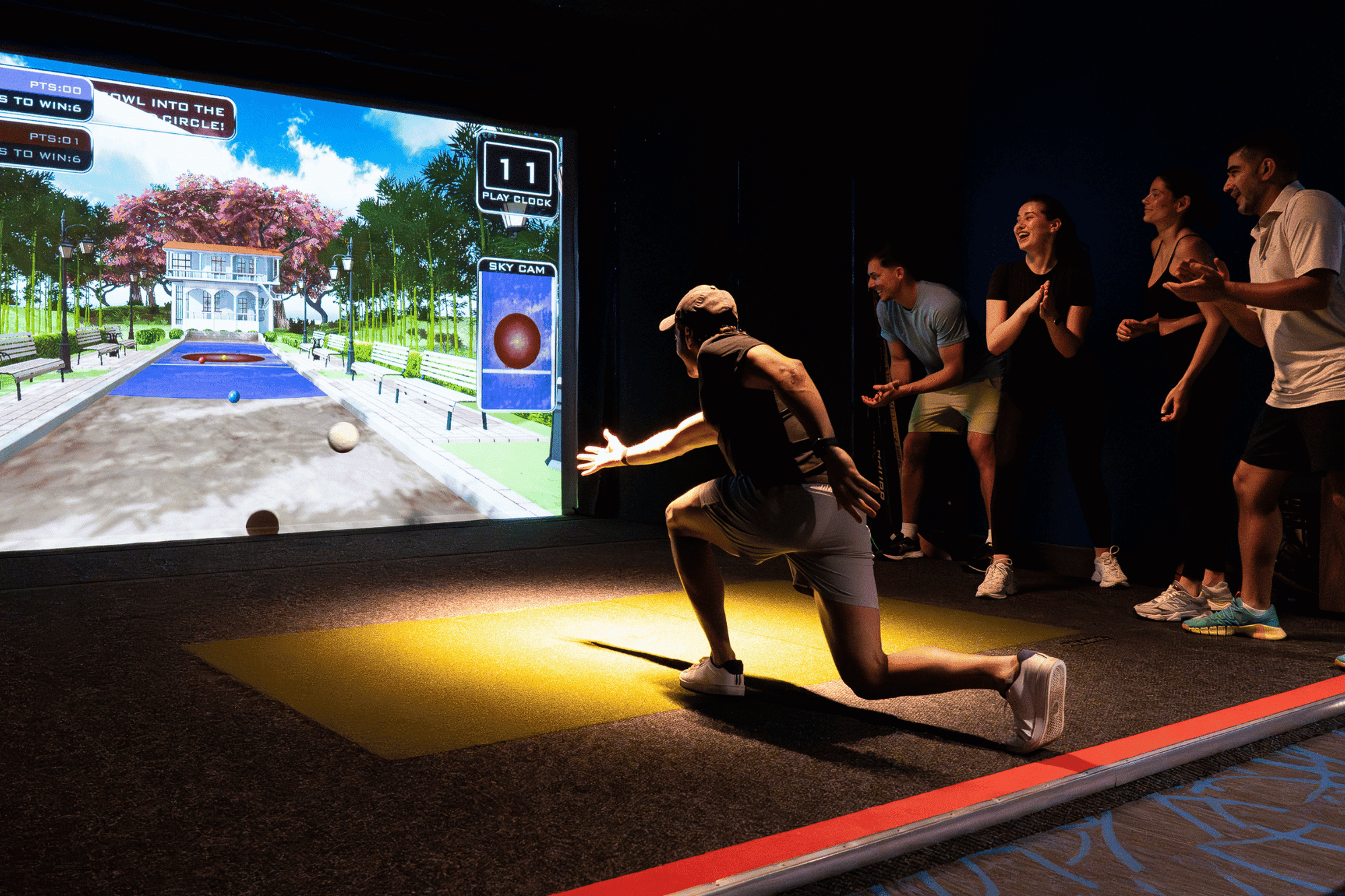 Guests at a sports simulator at Hotel X Toronto, with a player kneeling by the large screen as friends cheer nearby