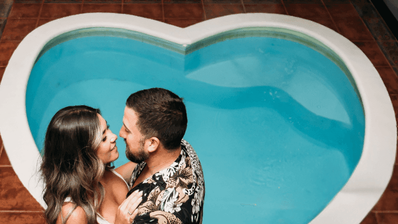 Couple standing close to each other by a heart shaped swimming pool at Cove Pocono Resorts