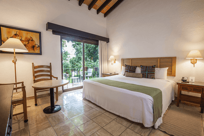 Cozy hotel room with king-size bed, chairs, desk, lamps, and sliding glass doors leading to a balcony.